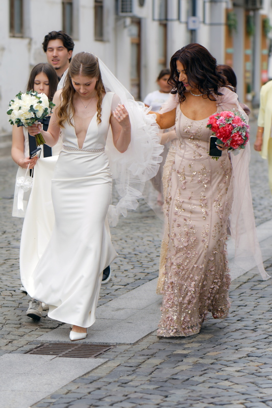 19 - A bride in a white wedding dress walking down a cobbled street with a person beside her